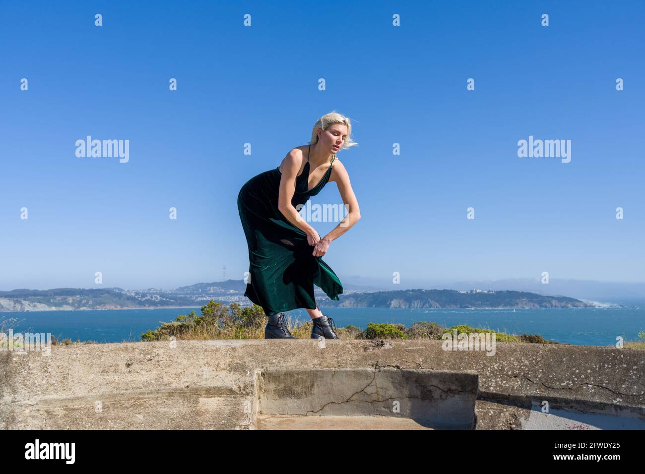 Mode dans des endroits inhabituels, femme en robe pleine longueur debout dans les ruines de la batterie d'arme à feu Banque D'Images