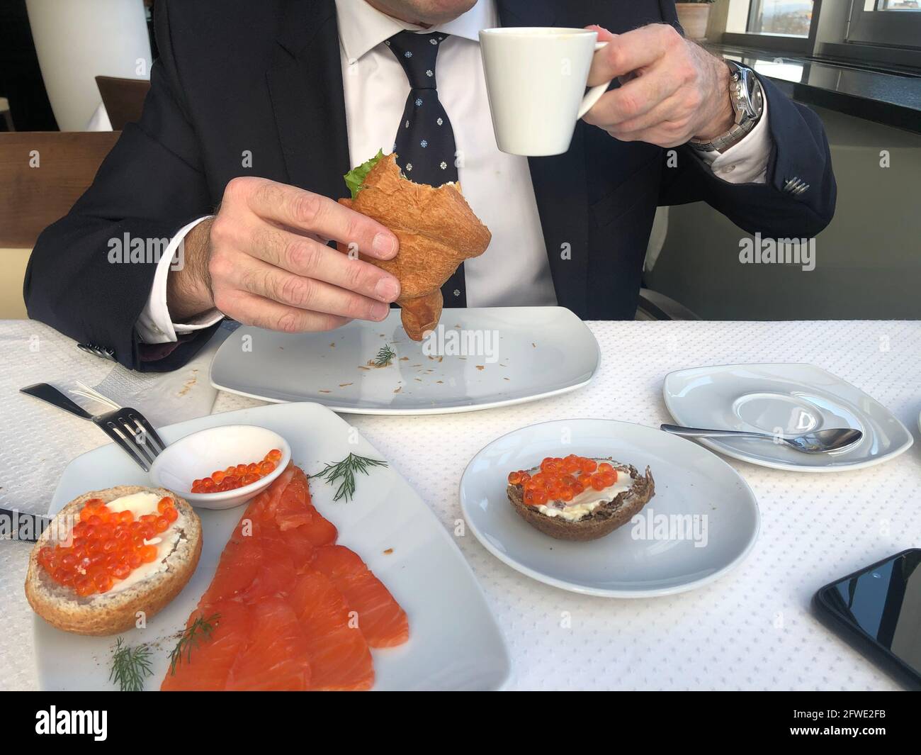 Homme dans un costume d'affaires, cravate et chemise blanche est de prendre  le petit déjeuner, pause-café, une tasse de café, croissant avec saumon et  salade verte, sandwichs avec Photo Stock - Alamy