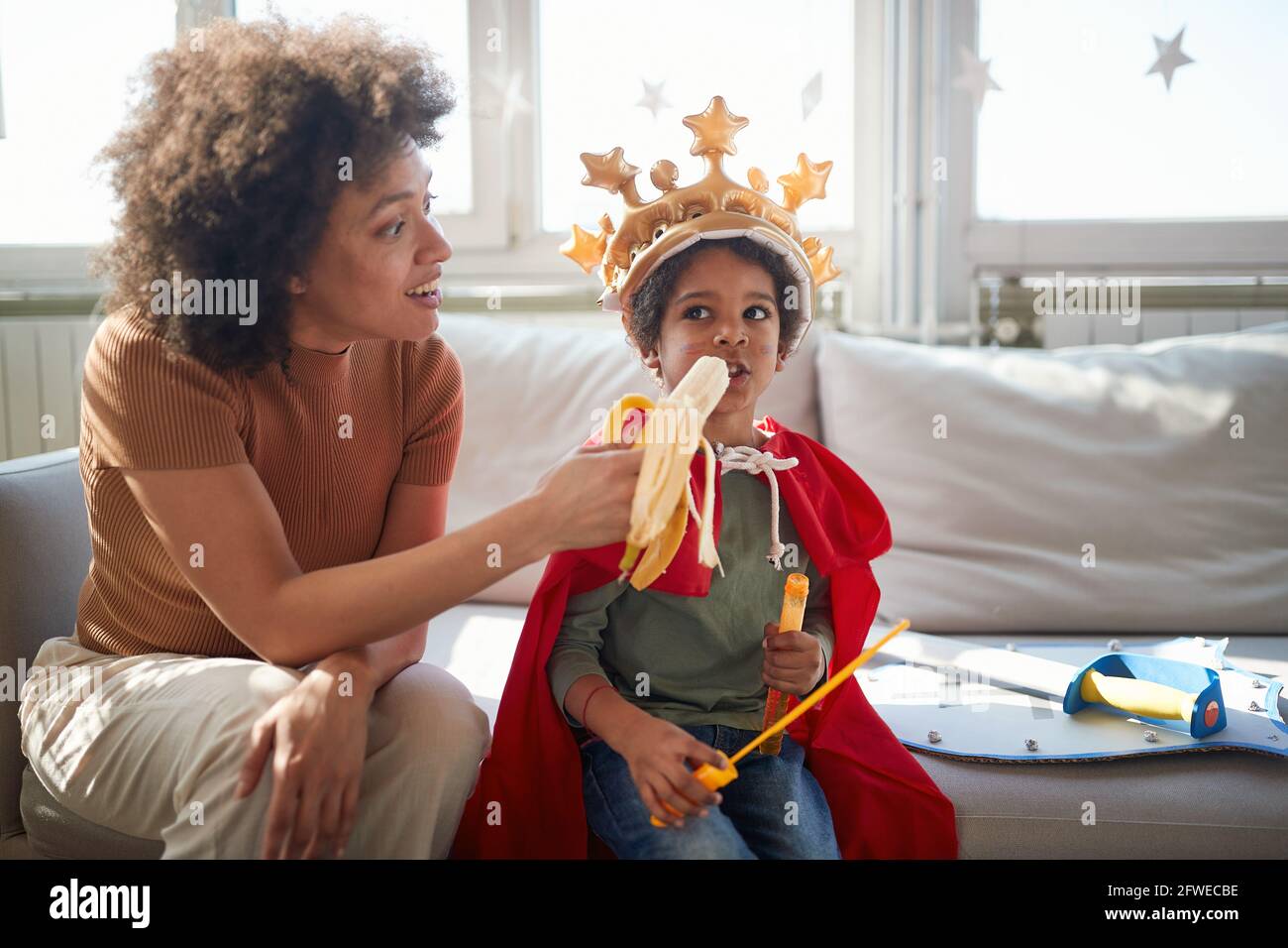 Une jeune maman nourrit son petit fils avec la banane tout en jouant dans une atmosphère détendue à la maison ensemble. Famille, ensemble, amour, temps de jeu Banque D'Images