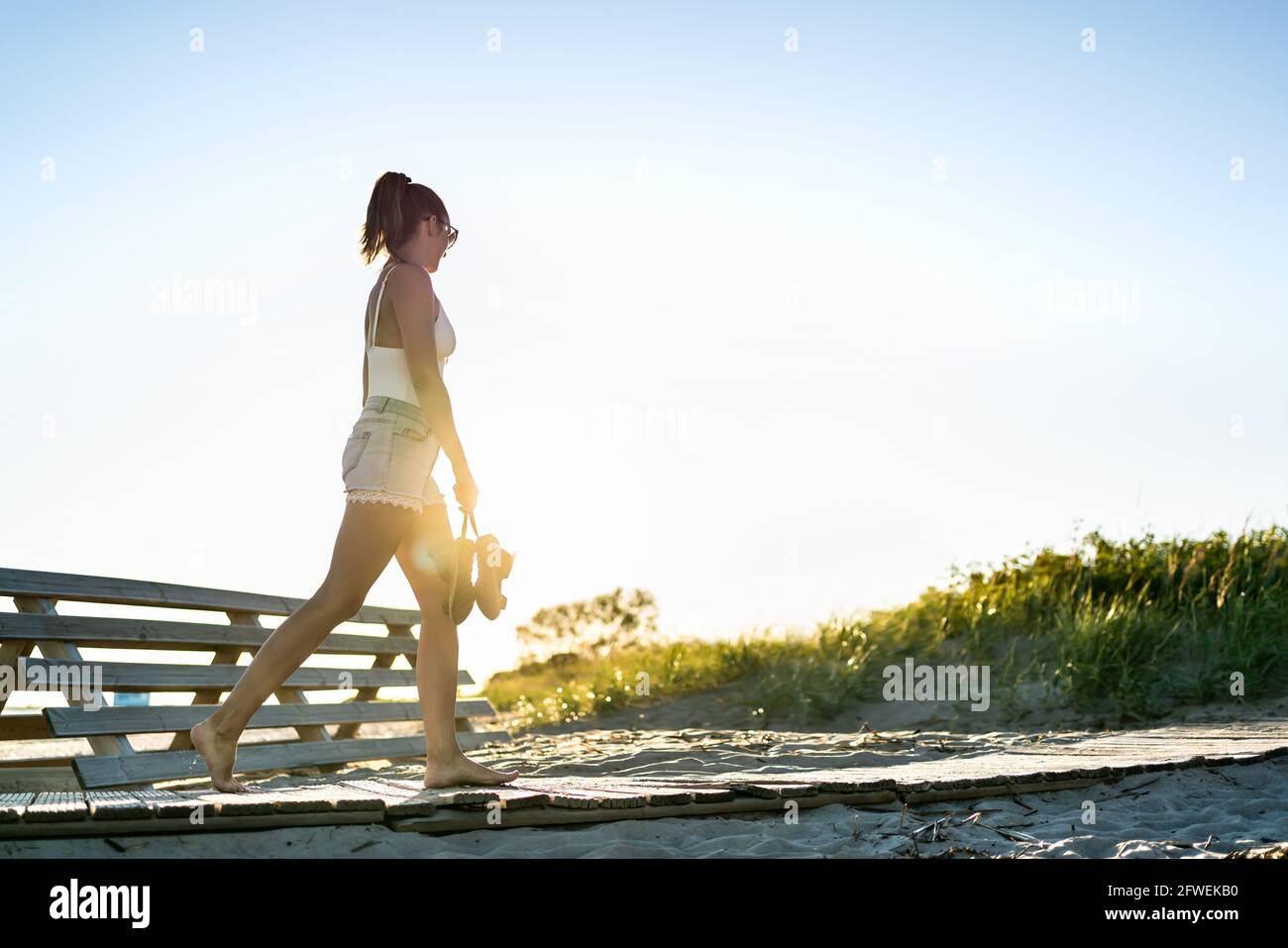 Promenade en soirée d'été sur la promenade de la plage à l'aube. Jeune femme solitaire triste en mélancolie ou en solitude au coucher du soleil. Presque la silhouette d'une personne. Banque D'Images
