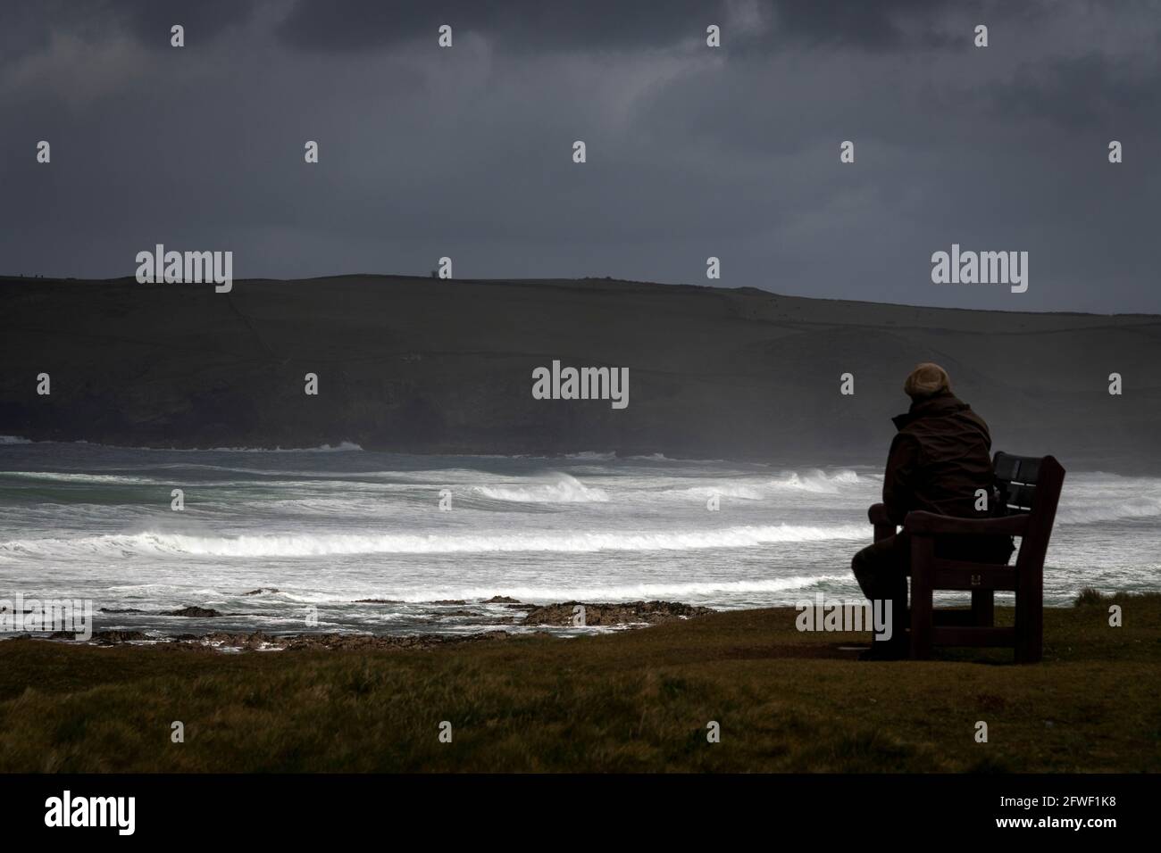 Un homme regarde la mer depuis un banc côtier lors d'une tempête à Polzeath, en Cornouailles. Banque D'Images