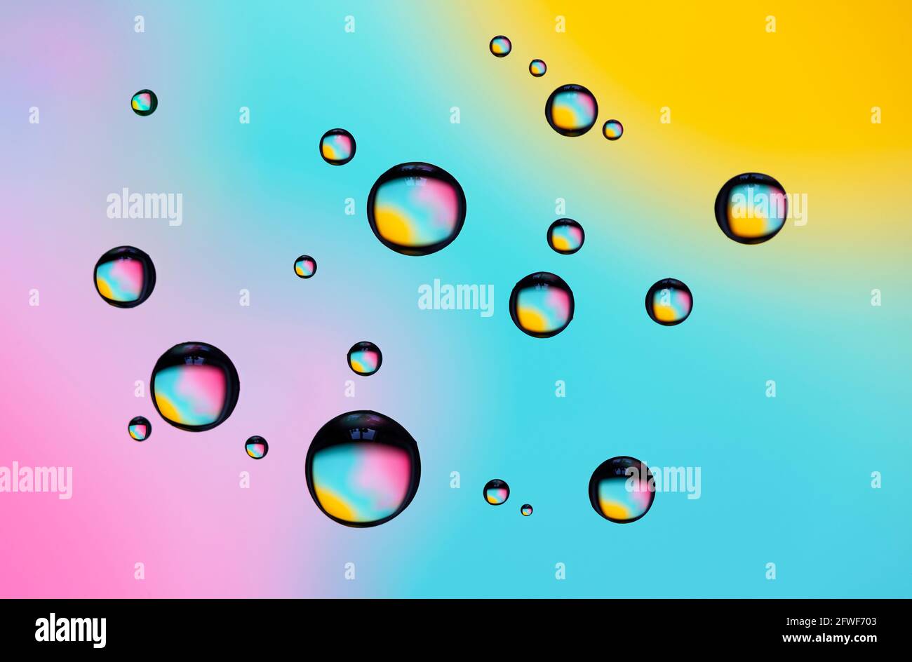 Beaux effets de diffraction de couleur des gouttelettes d'eau sur le verre contre un arrière-plan multicolore Banque D'Images