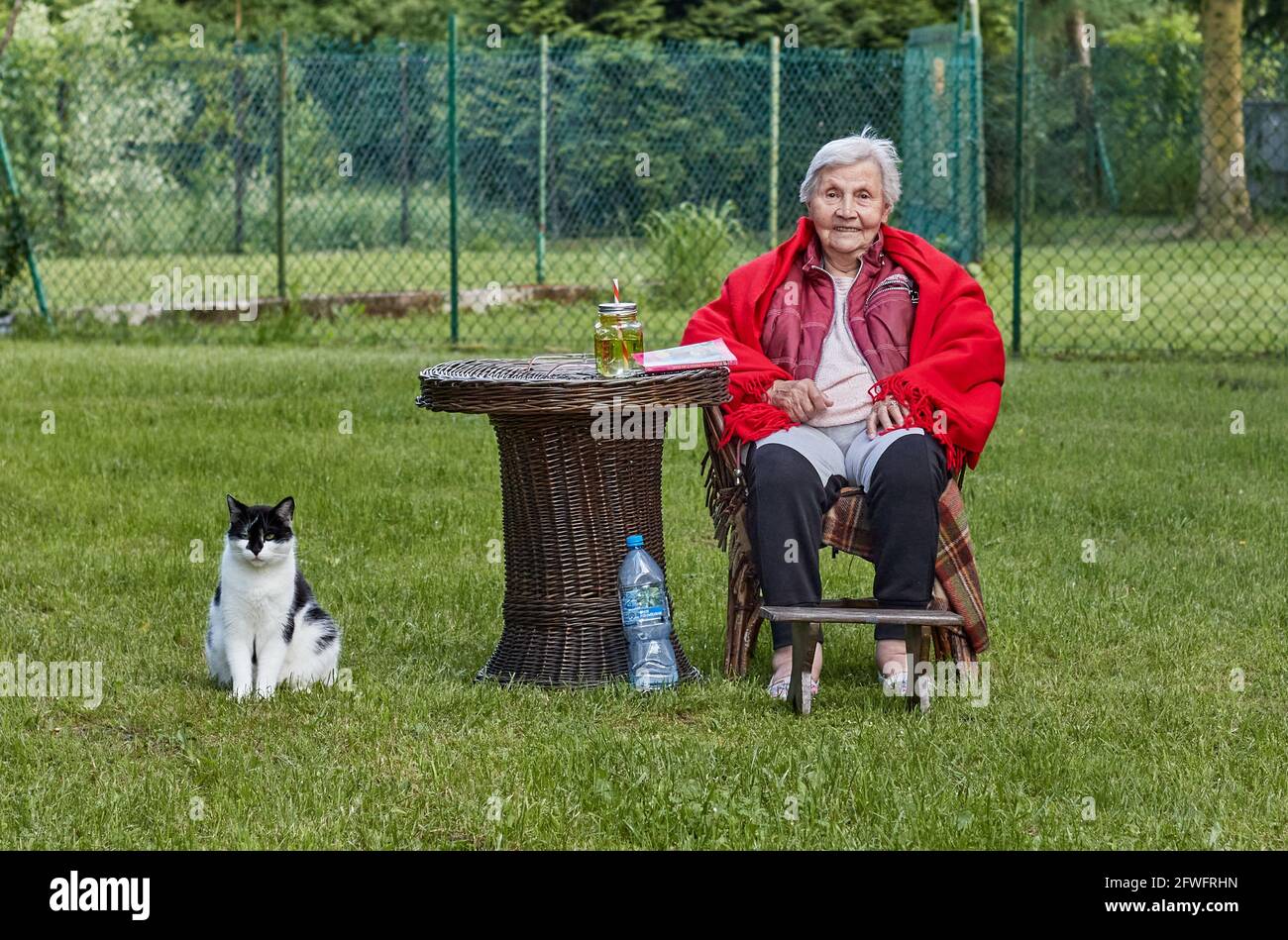 Femme âgée assise à la retraite, dans un poncho rouge avec gardien de chat noir et blanc Banque D'Images