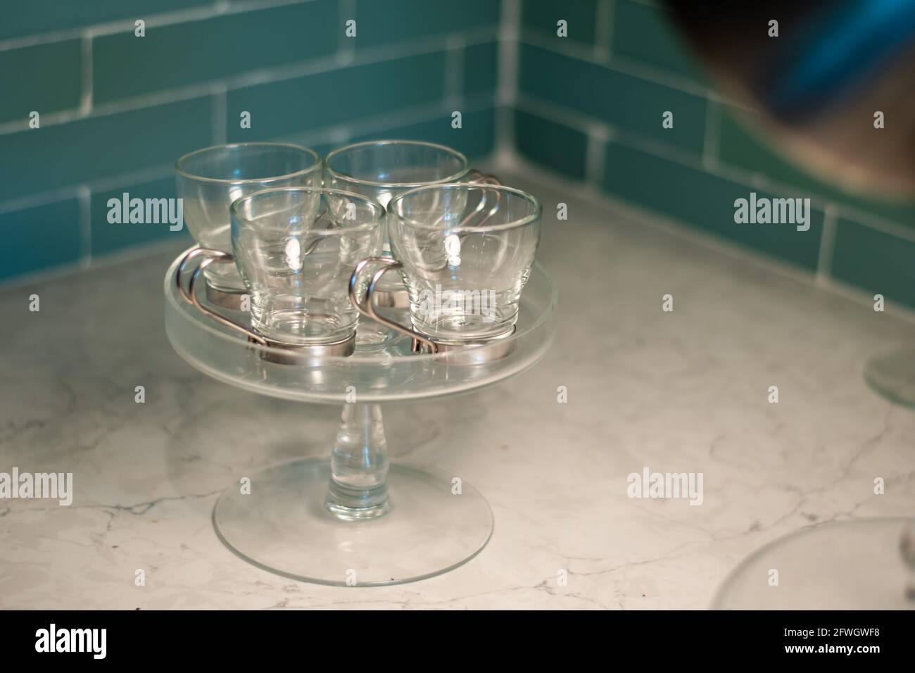 Divers verres - y compris des verres à espresso, un plateau à gâteaux et des pichets devant un carrelage intérieur moderne. Banque D'Images