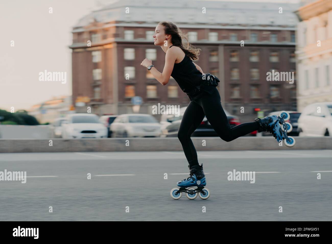 Une femme roule sur des rouleaux se déplace très rapidement vêtue en activité wear aime être photographié en mouvement pose en milieu urbain placez engagé dans Banque D'Images