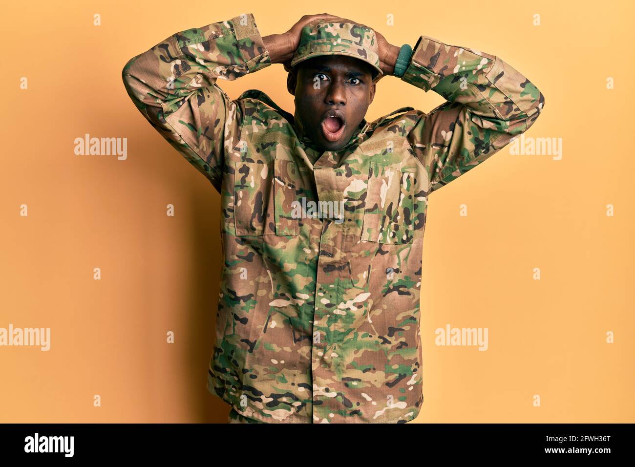Jeune afro-américain portant l'uniforme de l'armée folle et effrayée avec les mains sur la tête, peur et surprise de choc avec la bouche ouverte Banque D'Images