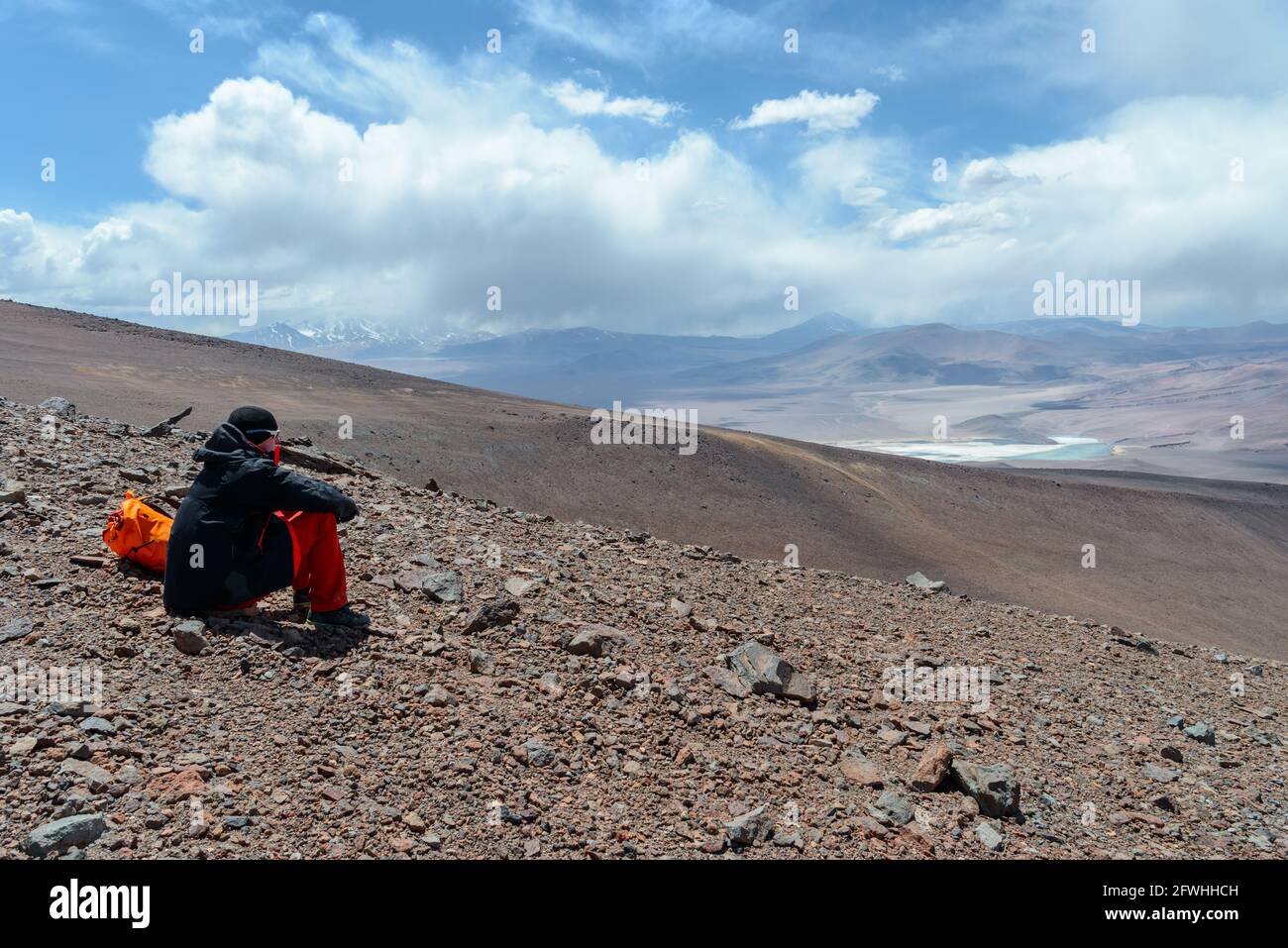 Jeune homme ayant un repos et regardant le paysage aride étonnant pendant son ascension du volcan Siete Hermanos au coeur du désert d'Atacama Banque D'Images