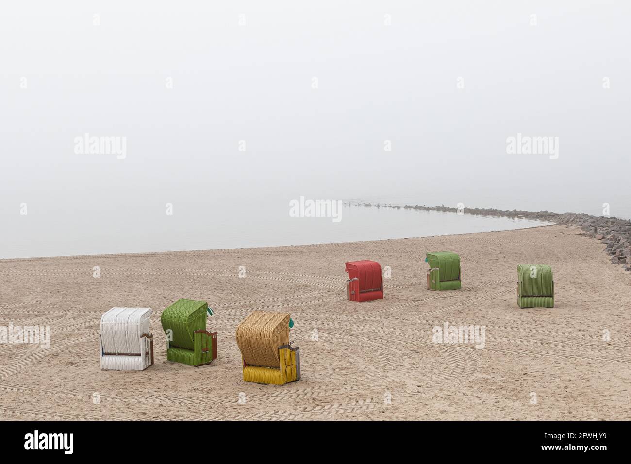 Six chaises de plage colorées sur la plage de Föhr par temps brumeux. Les chenilles du tracteur forment des cercles sur le sable et autour des chaises de plage. Banque D'Images