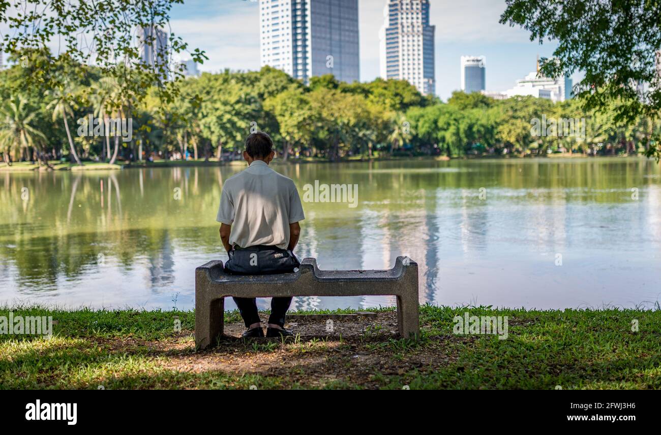 Un vieil homme non identifié est assis seul dans le parc Lumpini, vue arrière d'un vieil homme maigre assis sur un siège en pierre, grand étang i Banque D'Images