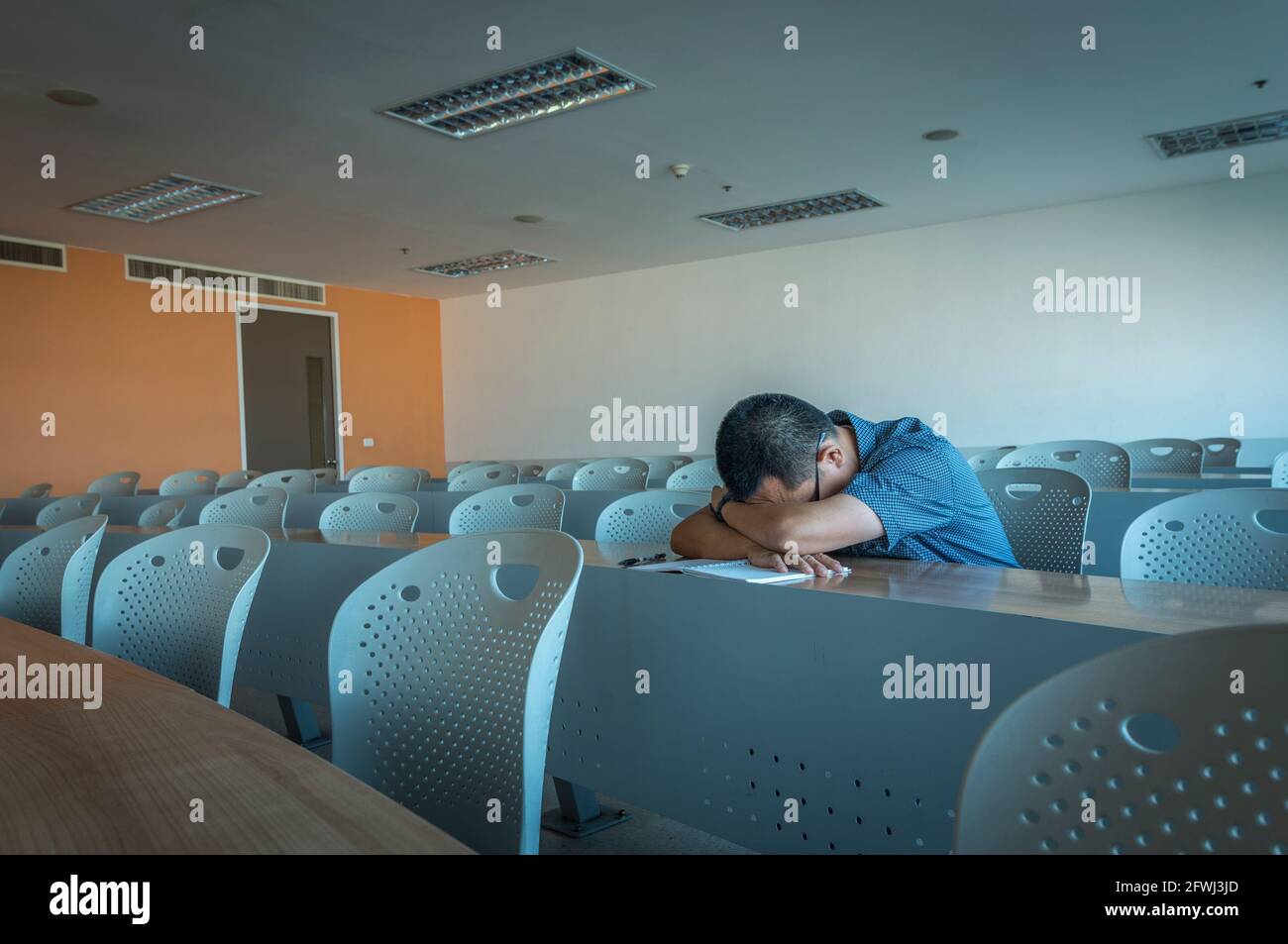 Un homme asiatique d'âge moyen est en train de se mettre seul sur le long bureau dans la salle de classe, vue en perspective, le reste des chaises sont vides. Banque D'Images