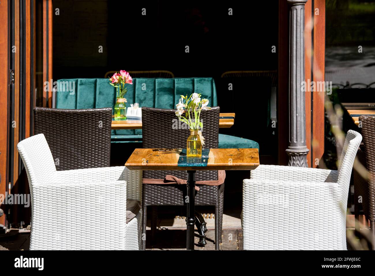 terrasse de café extérieure avec tables en bois et vase en verre et une  fleur et chaises en osier dans blanc et brun à l'extérieur du restaurant  avec des sièges vides Photo