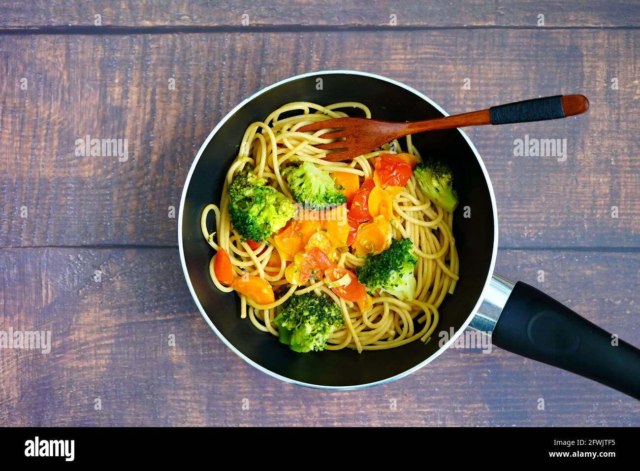 Une cuisine maison saine: Spagetthi avec des légumes (brokkoli, tomates, carottes) dans une poêle à frire avec une cuillère en bois. Banque D'Images