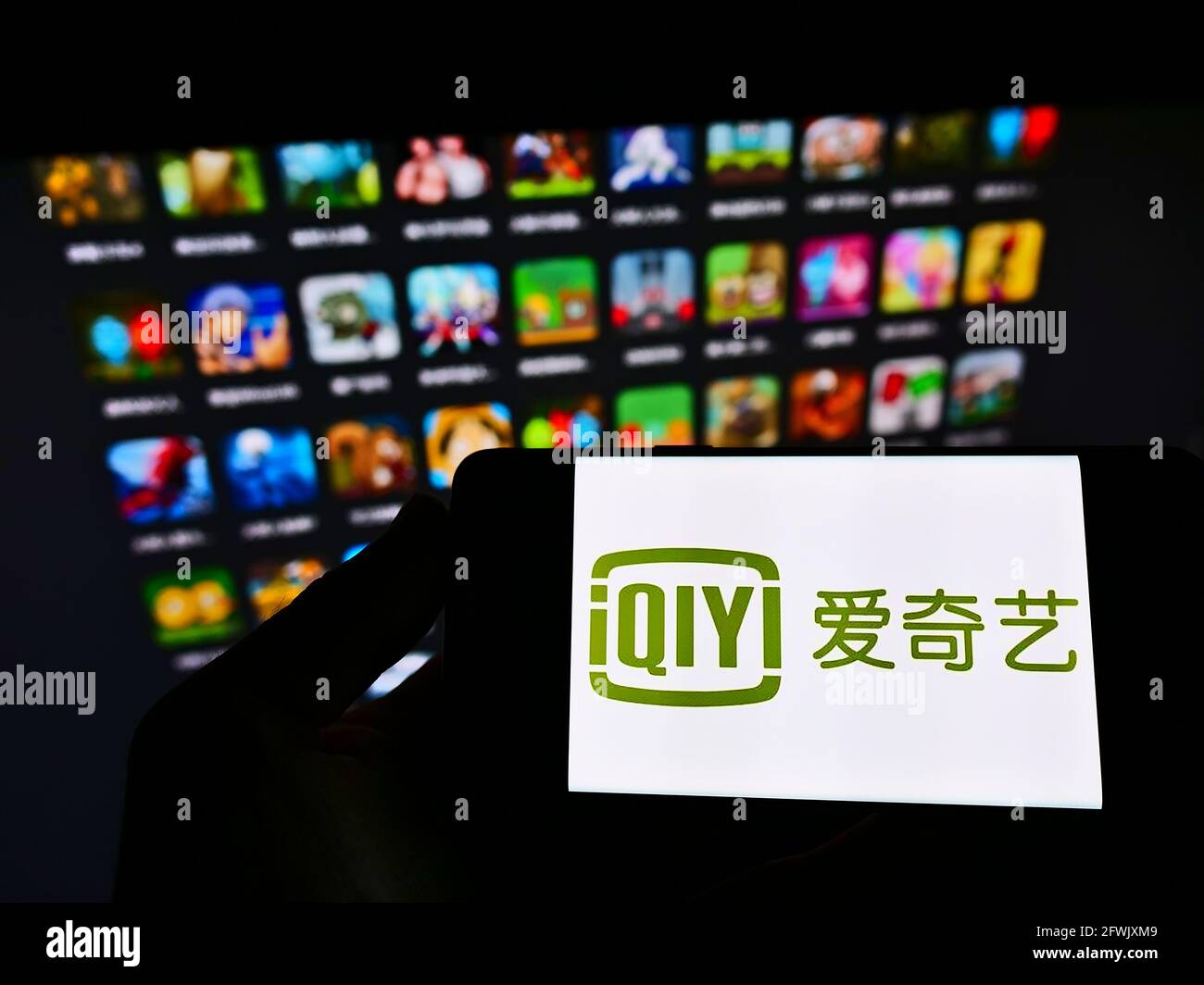 Personne tenant un téléphone mobile avec le logo de la société chinoise de plate-forme vidéo en ligne iQIYI Inc. À l'écran en face de la page Web. Mise au point sur l'affichage du téléphone. Banque D'Images