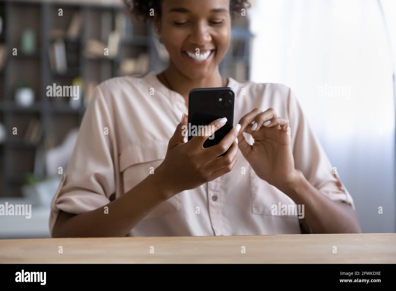 Jeune femme africaine souriante utilisant un smartphone à l'intérieur. Banque D'Images