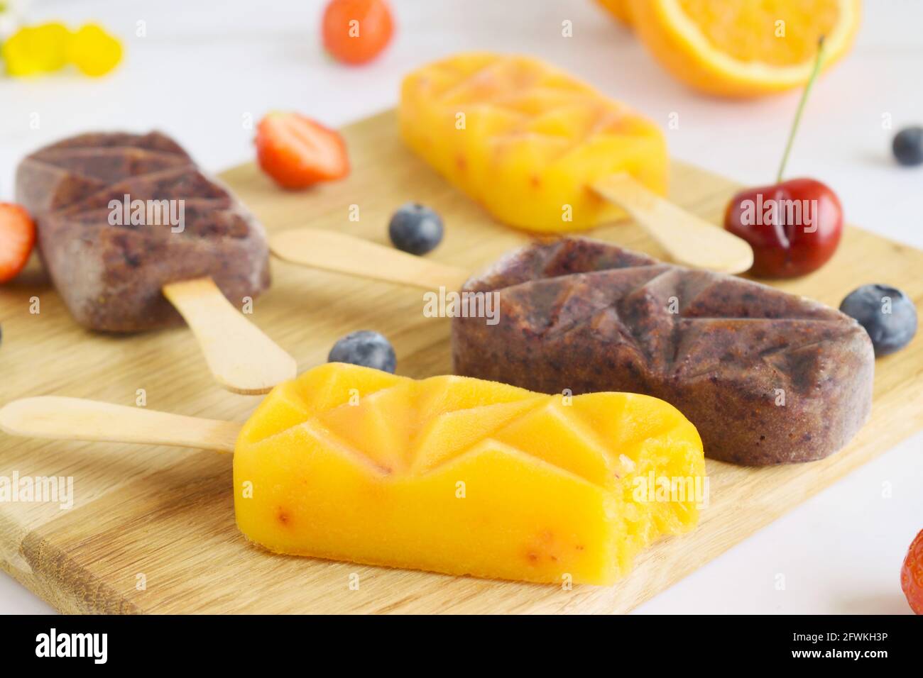 Groupe de framboises maison, cerises, fraises, oranges, pop-sicles vanille sur un paddle-board, jus de fruits surgelés, concentré sélectif, ba de marbre blanc Banque D'Images