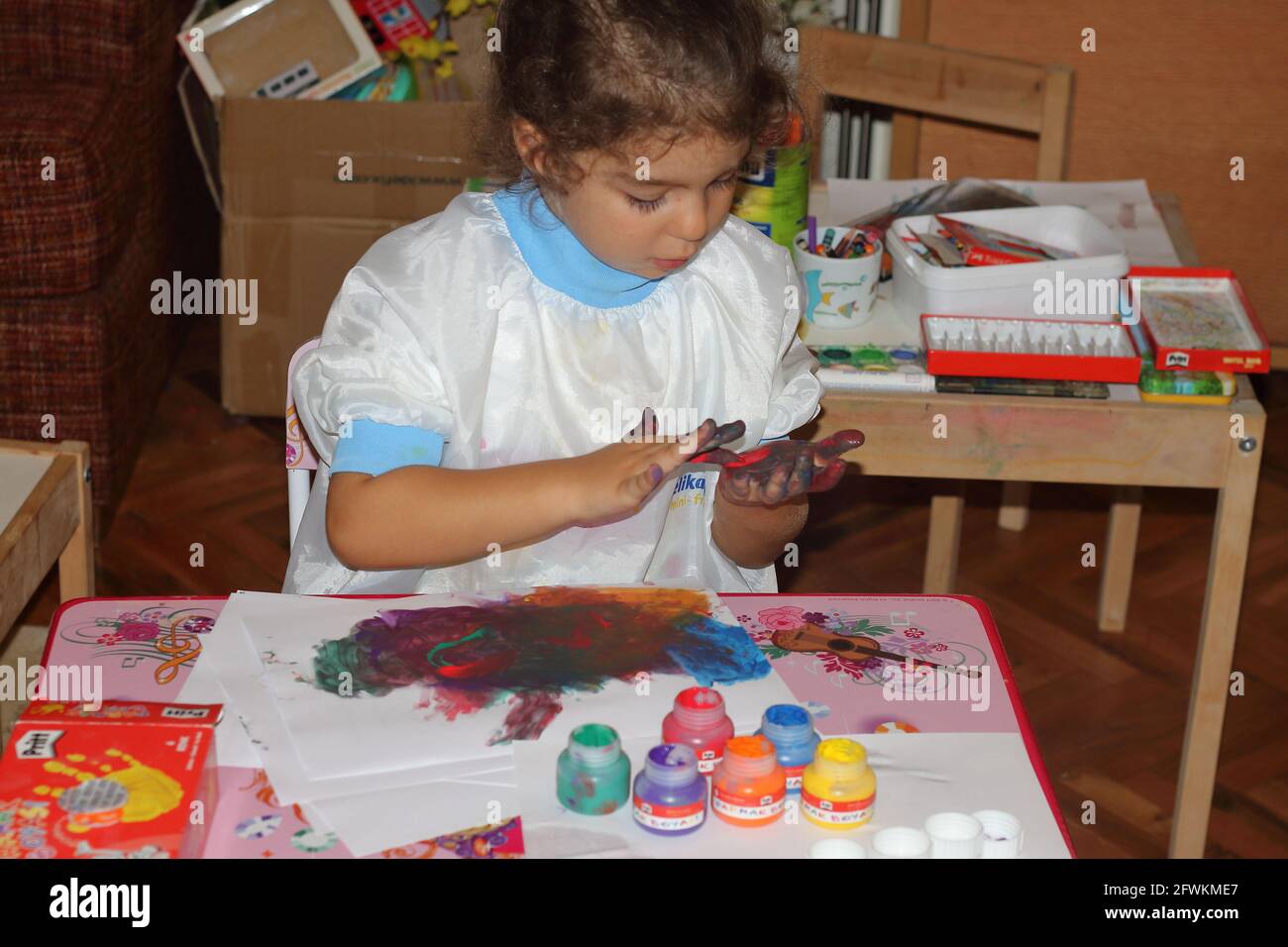 lllittle fille peintre curieusement mélanger les couleurs, mais en utilisant ses mains au lieu de la palette Banque D'Images