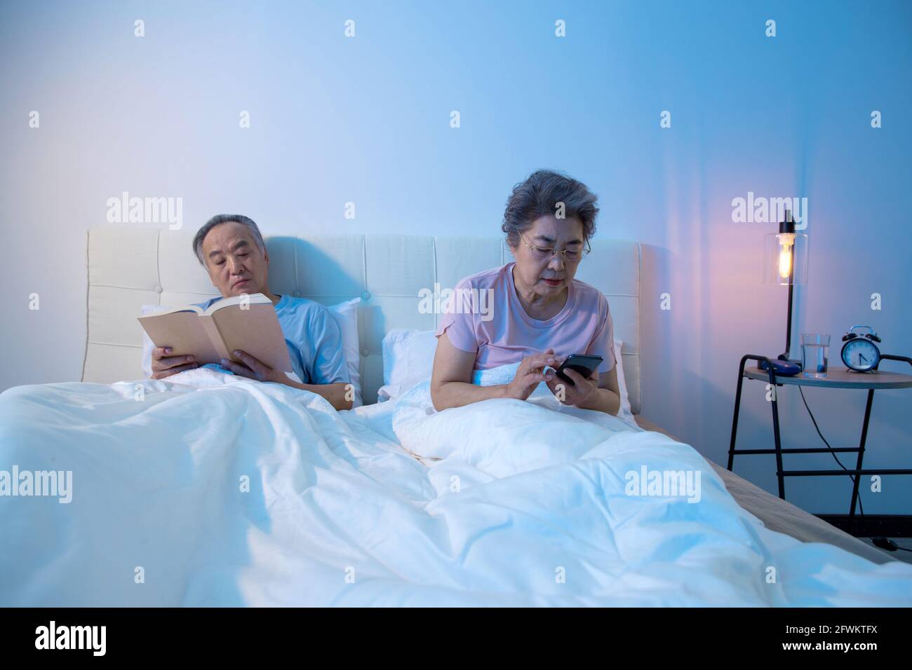 Un couple âgé s'est assis au lit pour lire un livre voir un téléphone mobile Banque D'Images