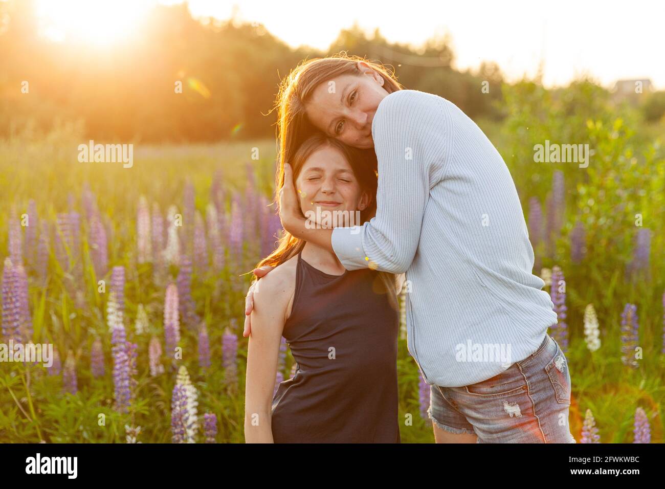 Jeune mère embrassant son enfant à l'extérieur. Femme et adolescente sur le terrain d'été avec fleurs sauvages fleur de fond vert. Bonne famille maman et Banque D'Images