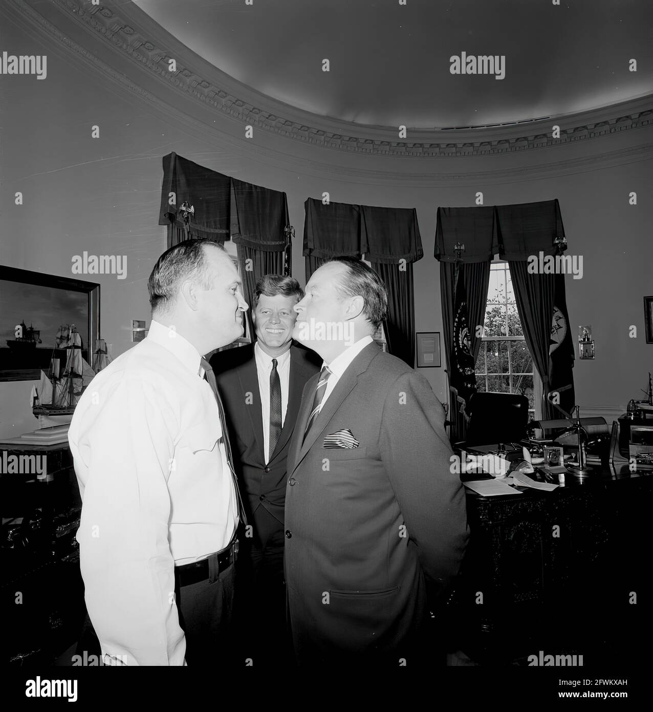 Le président John F. Kennedy rit lors d'une visite avec l'acteur et  comédien Bob Hope (à droite, face à l'officier de police de la Maison  Blanche, le soldat Robert Suggs, Jr.), dans
