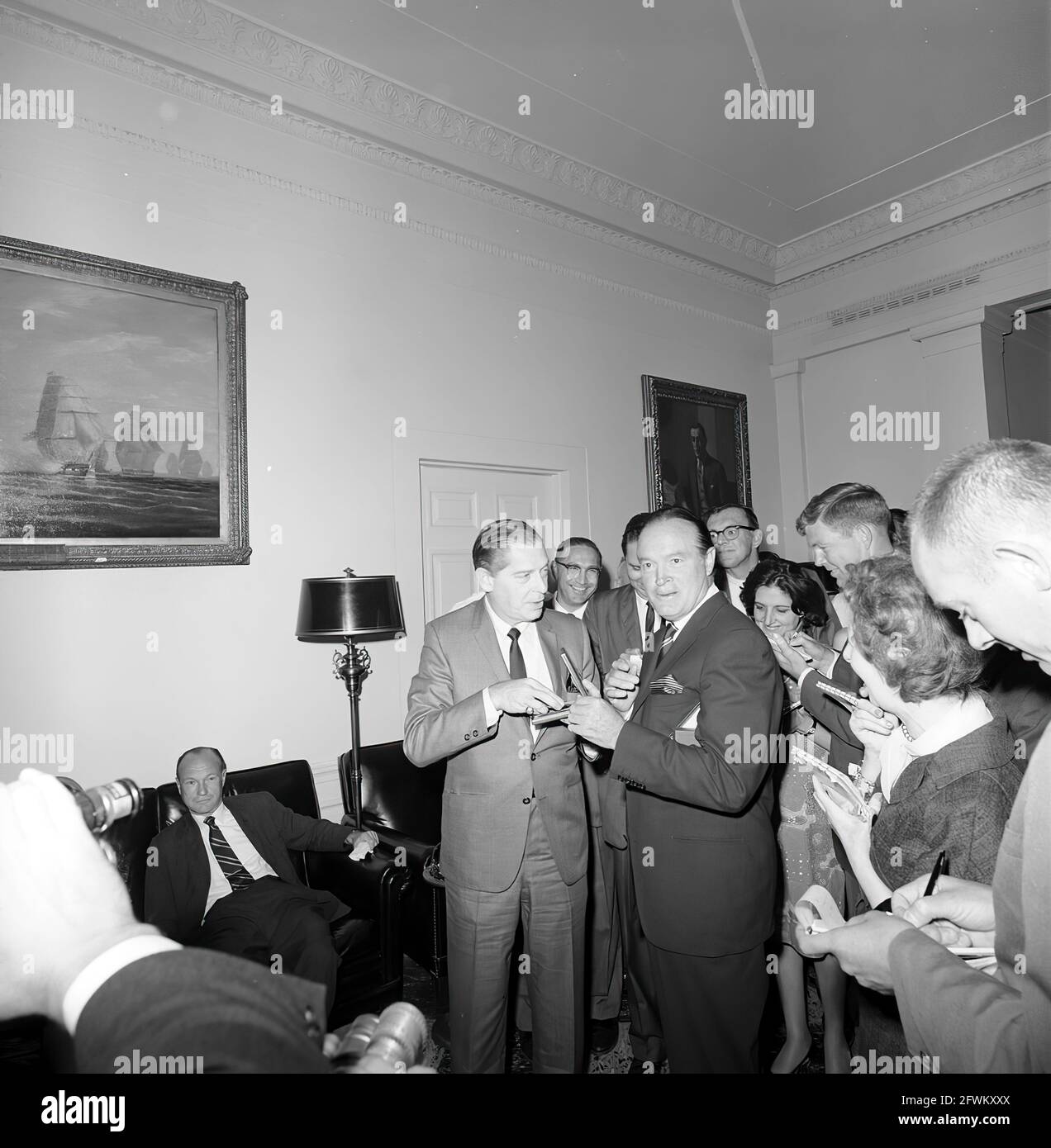 L'acteur et comédien, Bob Hope, montre son camarade comédien, Milton Berle, sa Médaille d'or du Congrès, qui lui a été remise plus tôt dans la journée par le Président John F. Kennedy en reconnaissance de ses services au pays en tant qu'animateur pendant la Seconde Guerre mondiale Les journalistes observent, notamment la correspondante de la Maison Blanche pour United Press International (UPI), Helen Thomas (debout derrière M. Hope) et la journaliste politique de Washington pour le New York Times, Tom Wicker (à droite de Mme Thomas). Hall de l'aile ouest, Maison Blanche, Washington, D.C. Banque D'Images