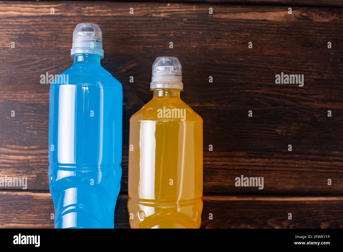 Deux bouteilles d'orange et de bleu sur fond de bois foncé, rétablissant l'équilibre eau/sel après l'entraînement sportif, gros plan. Banque D'Images