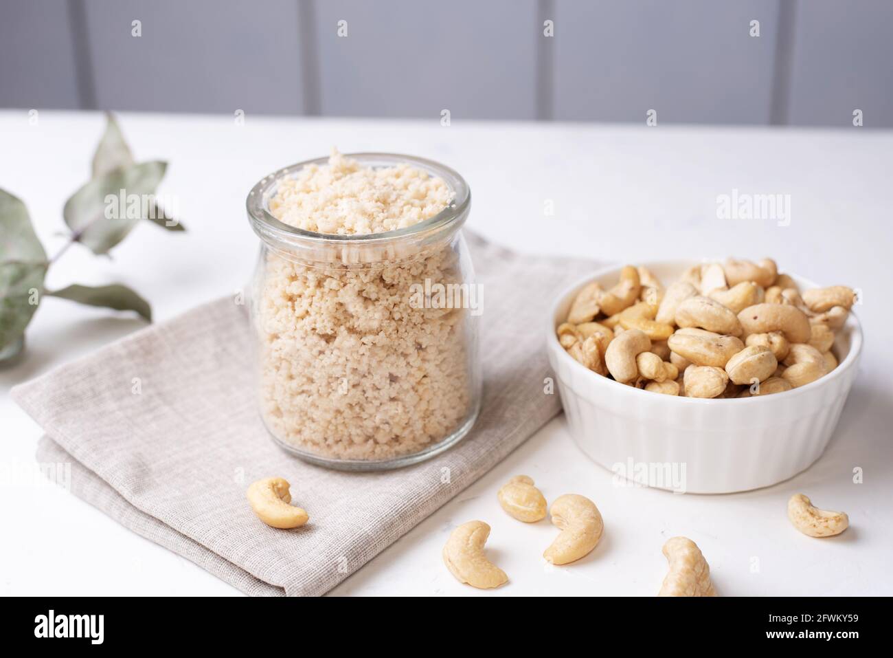 Parmesan vegan à base de noix de cajou moulées dans un pot en verre et noix de cajou sur fond blanc, plats végétariens, gros plan. Banque D'Images