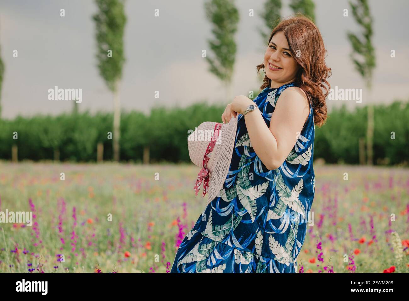 Portrait d'une femme enceinte tenant son chapeau plein sur le terrain de fleurs en été et profiter du temps chaud Banque D'Images