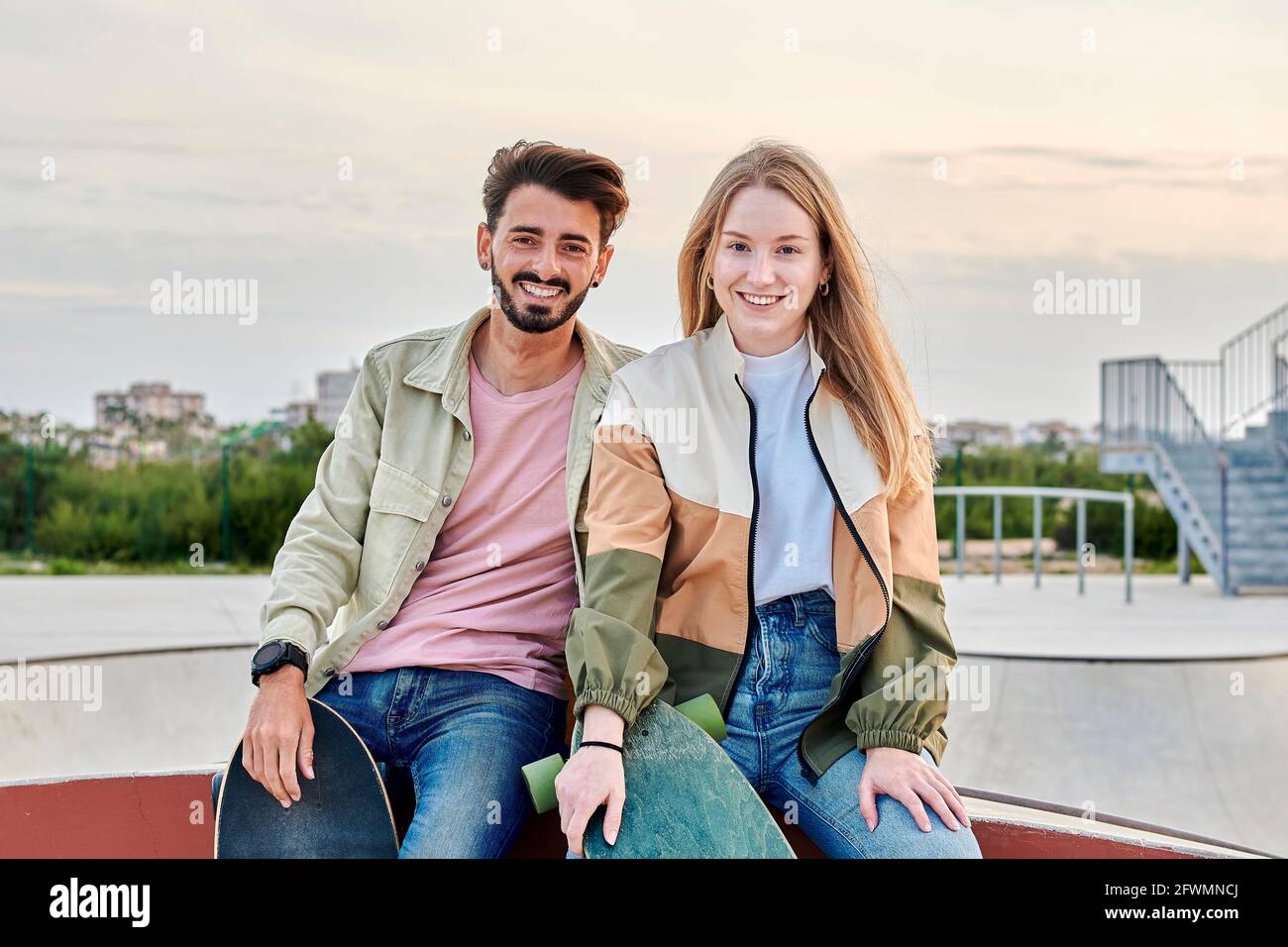 Un jeune couple multiracial regarde la caméra en souriant dans un parc de skate Banque D'Images