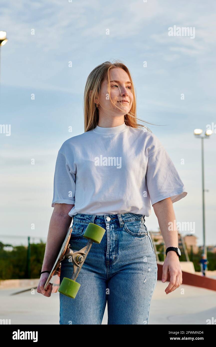 Jeune femme blonde souriant et s'amusant tenant un skateboard Banque D'Images