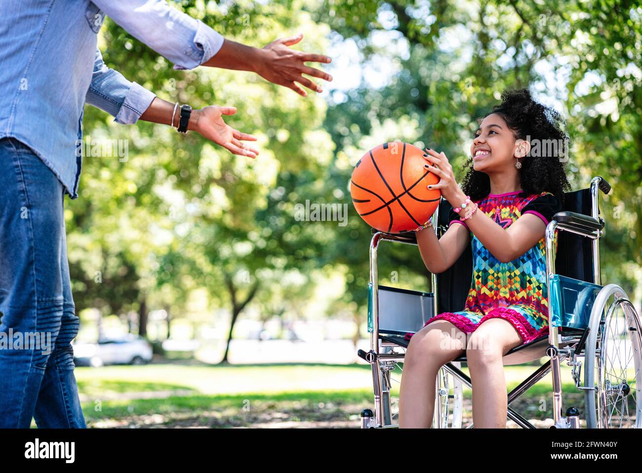 Petite fille en fauteuil roulant jouant au basket-ball avec son père. Banque D'Images