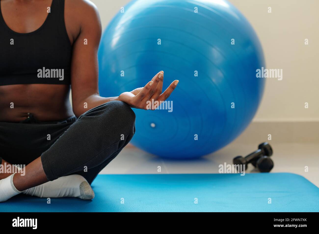 Image rognée de la jeune femme en forme méditant en position lotus après l'entraînement avec des haltères et des balles de fitnes Banque D'Images