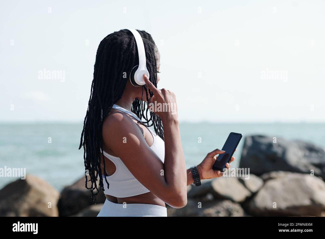 Sportswoman portant des écouteurs, elle choisit la bonne musique, livre audio ou podcast pour l'entraînement Banque D'Images