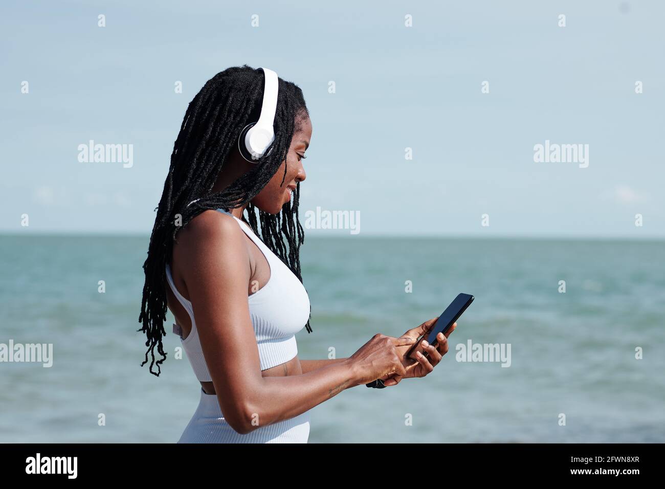Souriante, la jeune femme s'adapte dans un casque et choisit la musique pour elle transmission via une application sur un smartphone Banque D'Images