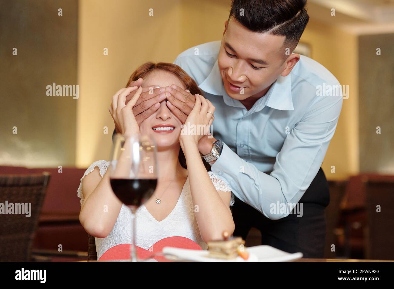 Beau jeune homme couvrant les yeux de la petite amie après l'avoir apporté délicieux dessert comme surprise Banque D'Images