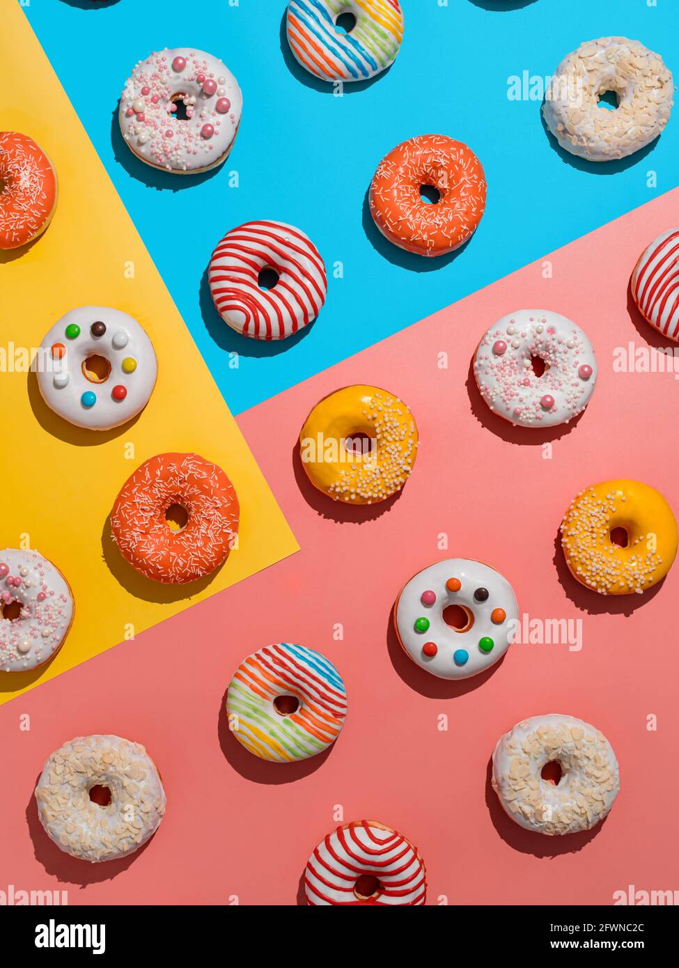 Assortiment de beignets vitrés colorés, vue sur le dessus. Design créatif à base de délicieux beignets glacés. Fond plat vertical avec beignets ou beignets multicolores. Fond bleu jaune rose. Lumière dure Banque D'Images