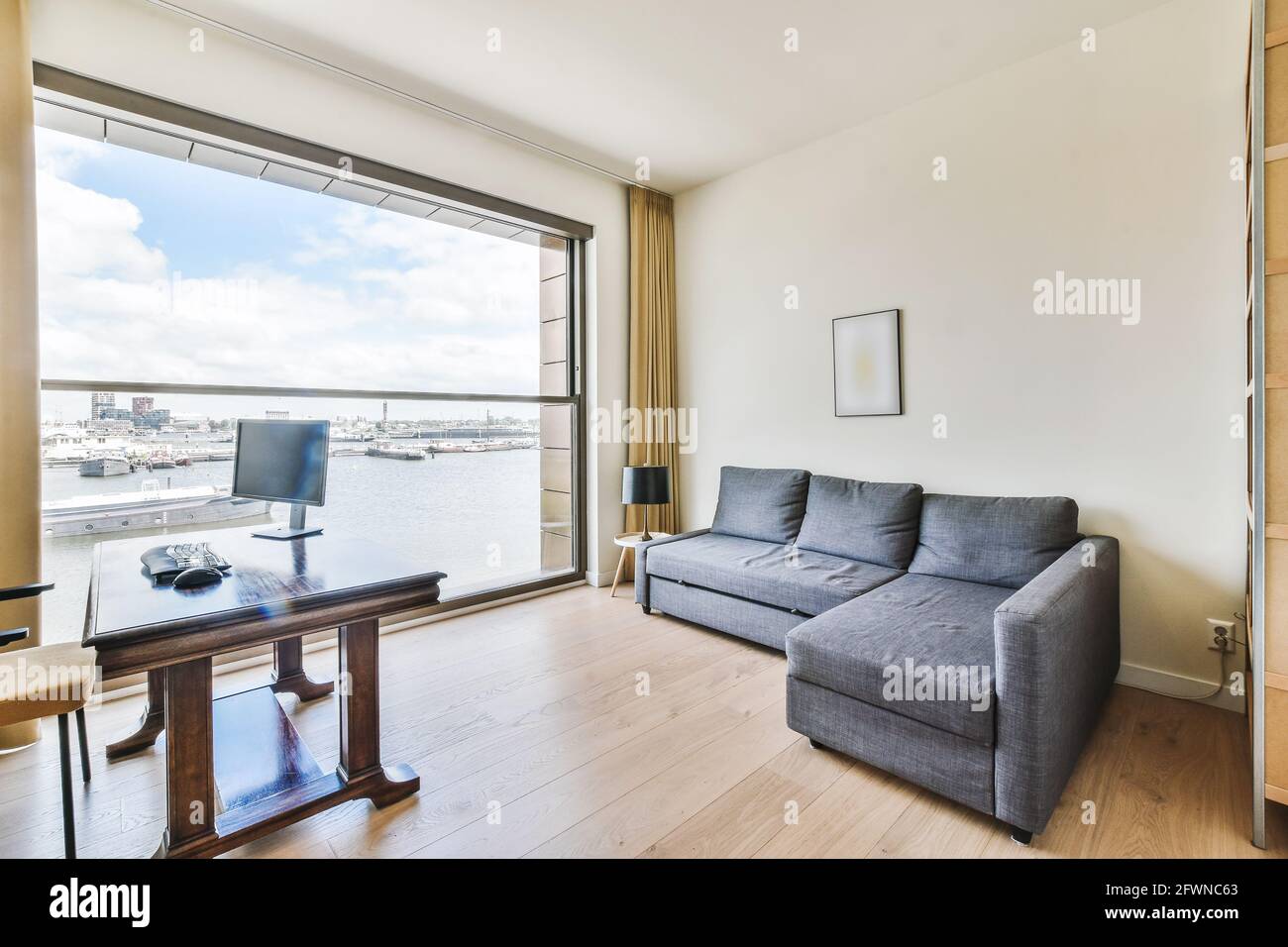 Design intérieur de l'espace de travail avec ordinateur sur table et gris canapé-lit dans la chambre avec vue sur le canal avec les bateaux dans un appartement de luxe moderne Banque D'Images