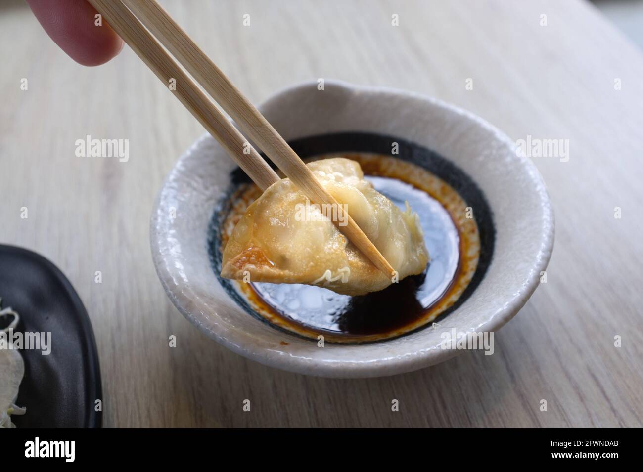 Main avec des baguettes tenant un morceau de gyoza frit Banque D'Images