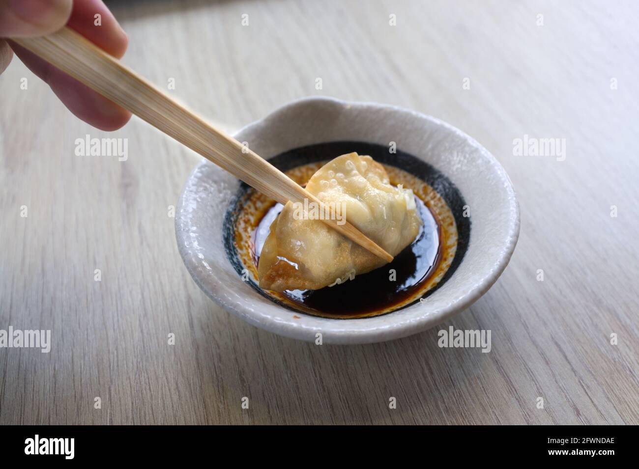 Main avec des baguettes tenant un morceau de gyoza frit Banque D'Images