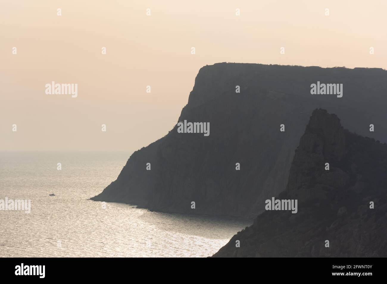Paysage marin neutre avec montagnes. Une belle silhouette de rochers sur le fond d'une mer argentée brillante. Brume de coucher de soleil beige. Au. Atmosphérique Banque D'Images