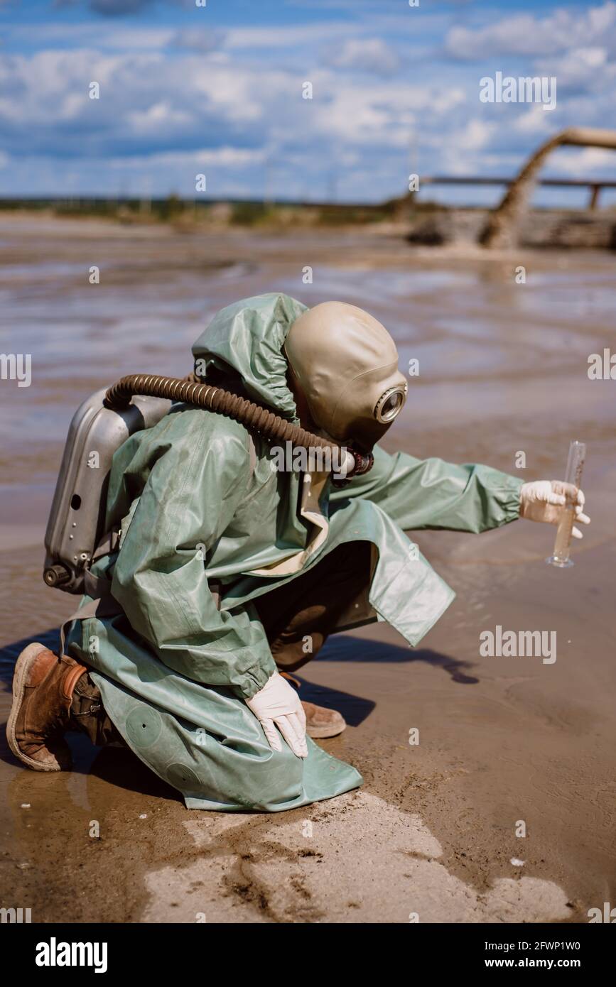 Un scientifique prélève un échantillon d'eau dans un réservoir après le rejet de déchets chimiques. Un homme dans un respirateur et une combinaison de protection verte de Banque D'Images