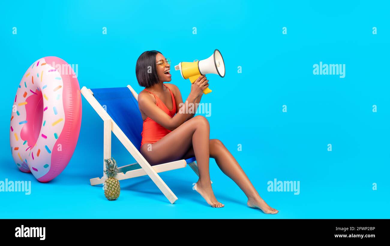 Offre incroyable. Jeune femme noire en maillot de bain assise dans un fauteuil de salon, criant dans le mégaphone, faisant l'annonce Banque D'Images