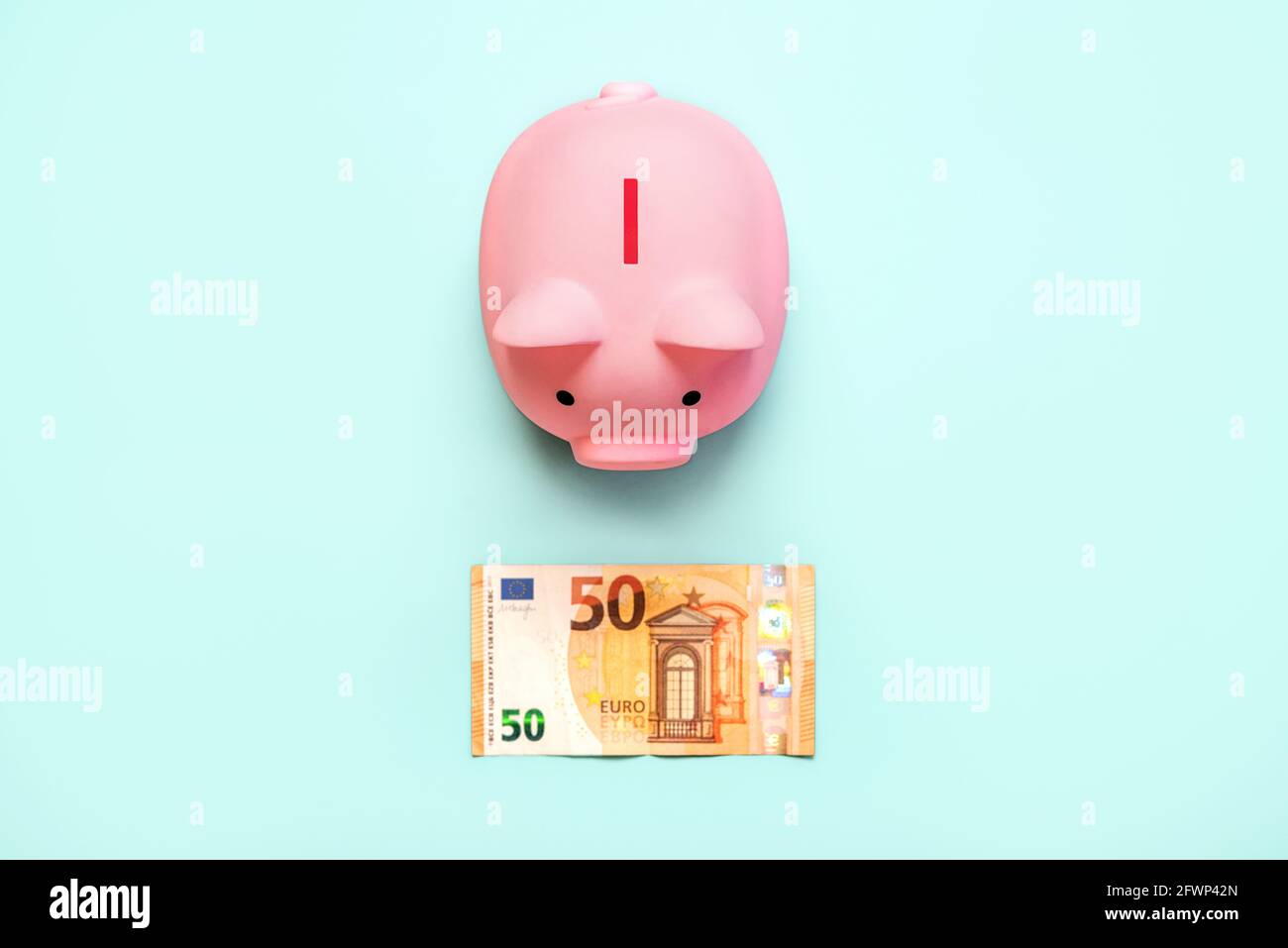 Vue de dessus de la banque de monnaie rose piggy avec une facture d'euro sur fond bleu Banque D'Images