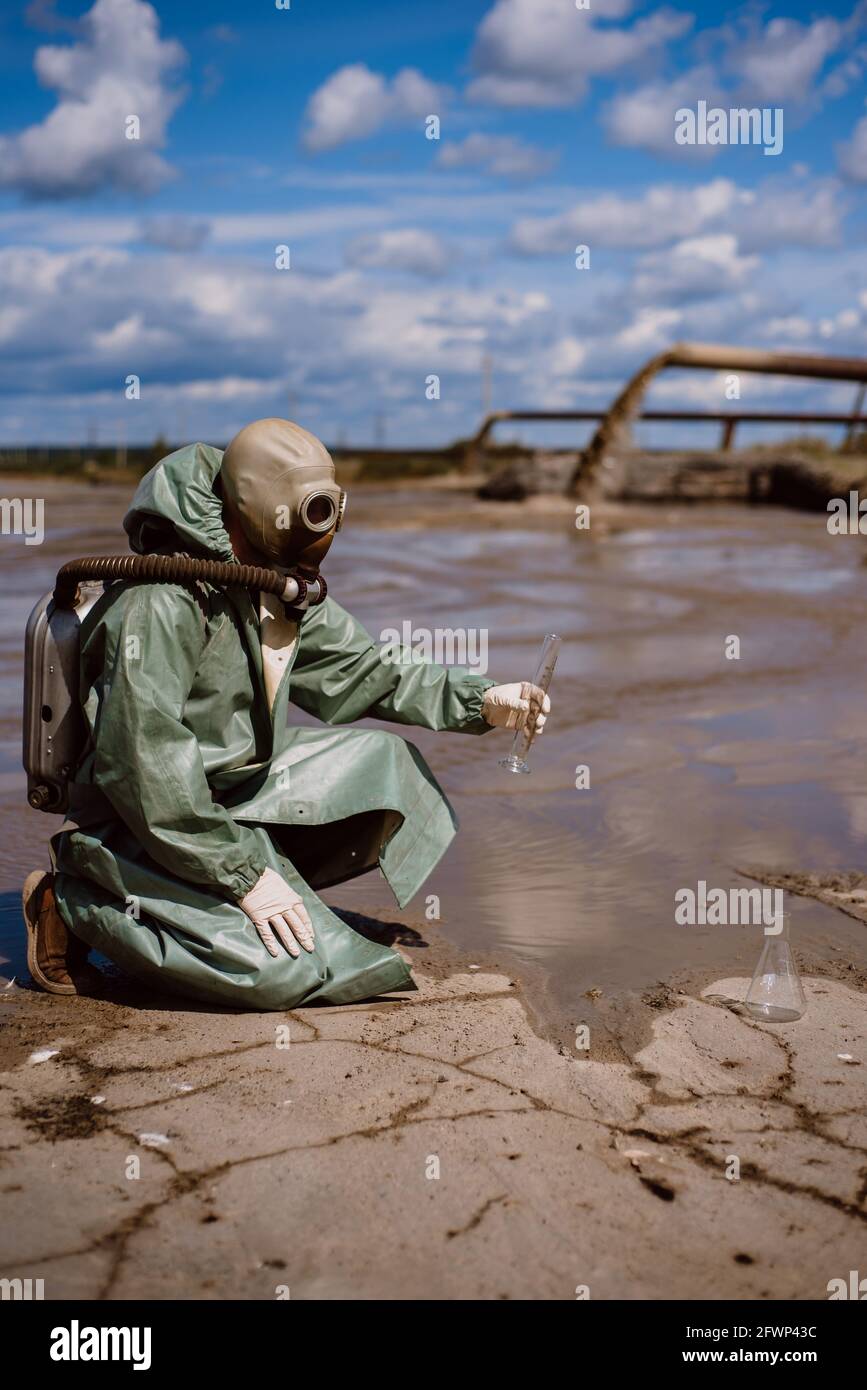 Un scientifique prélève un échantillon d'eau après le rejet de déchets chimiques. Un homme dans un respirateur et une combinaison de protection verte contre les radiations. Eau Banque D'Images