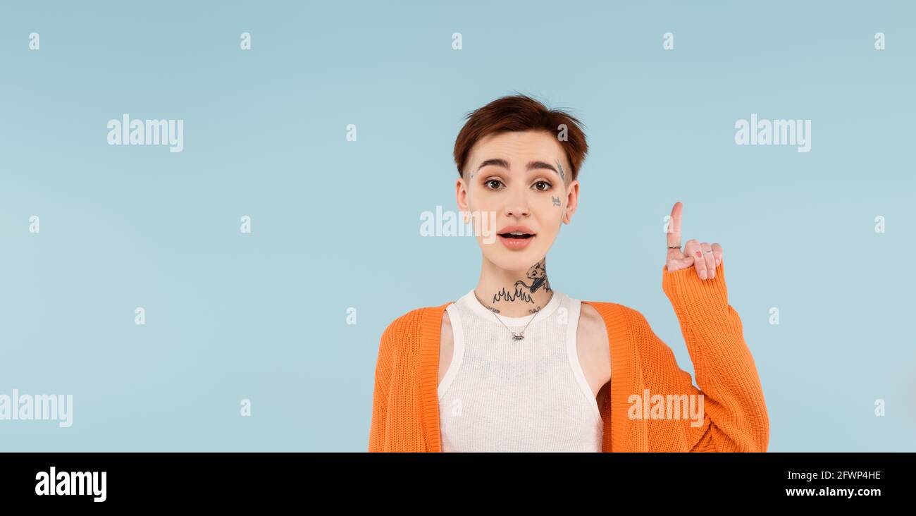 jeune femme tatouée stupéfait dans un gilet orange pointant vers le haut avec le doigt isolé sur la bannière bleue Banque D'Images