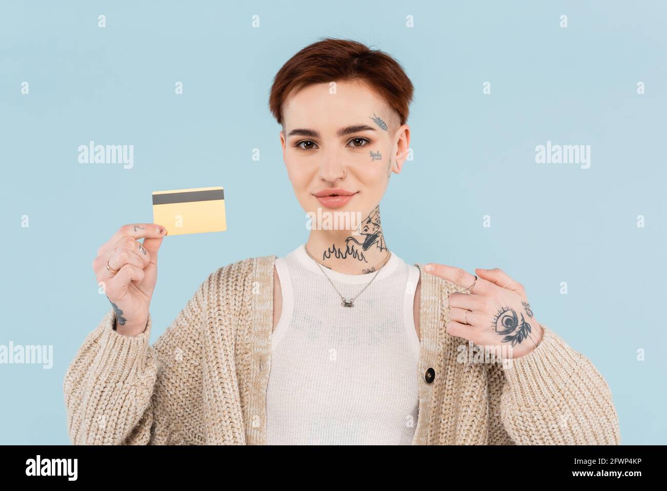 gaie et tatouée femme pointant du doigt à la carte de crédit isolé sur bleu Banque D'Images