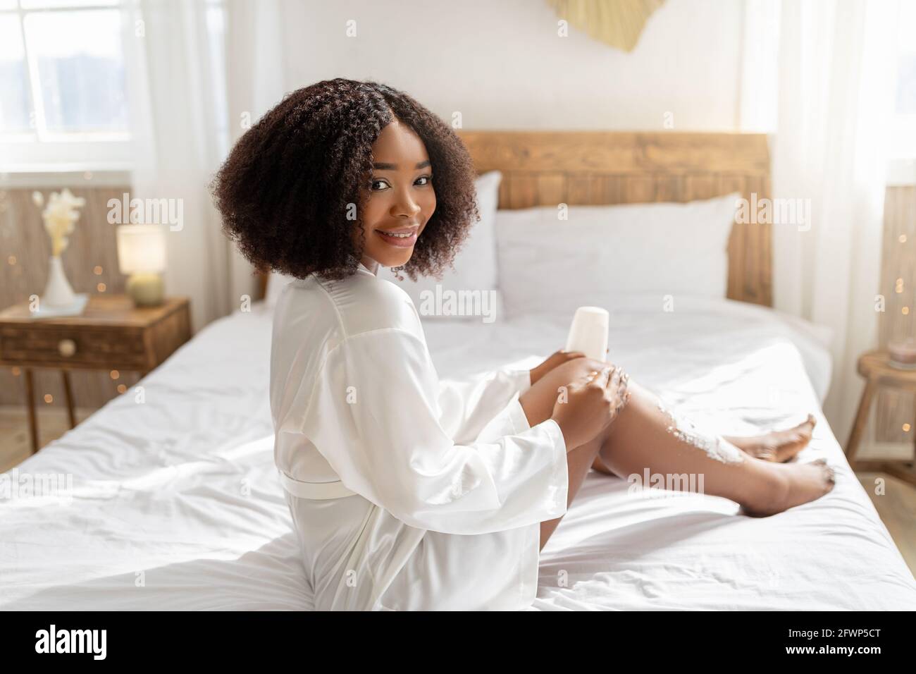 Jolie femme noire appliquant de la mousse de rasage sur ses jambes avant la procédure d'épilation domestique, se dorloter à la maison Banque D'Images