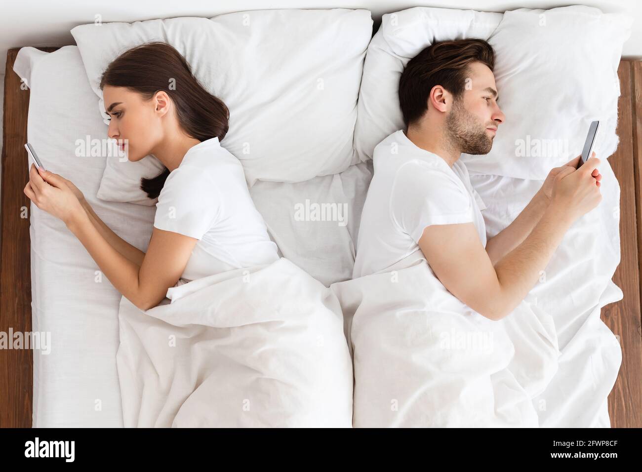Couple marié indifférent textant sur des téléphones couchés dos à dos intérieur, au-dessus de la vue Banque D'Images