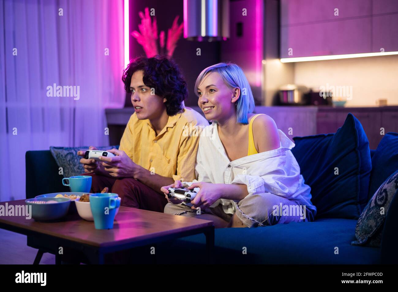 Belle fille à cheveux bleus et jeune homme tenant des contorllers de jeu jeux vidéo à la maison Banque D'Images