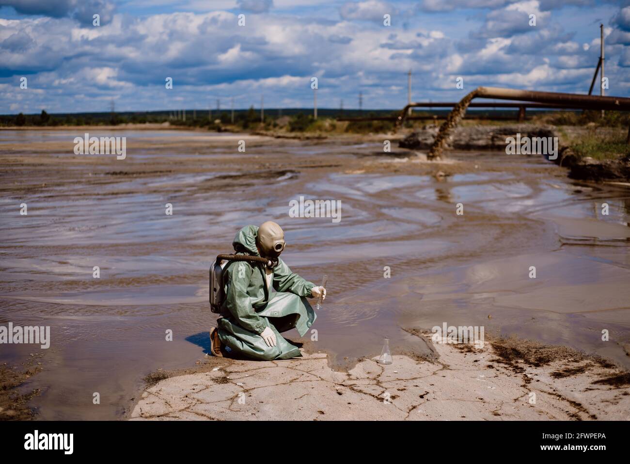 Un scientifique prélève un échantillon d'eau après le rejet de déchets chimiques. Un homme dans un respirateur et une combinaison de protection verte contre les radiations. Eau Banque D'Images