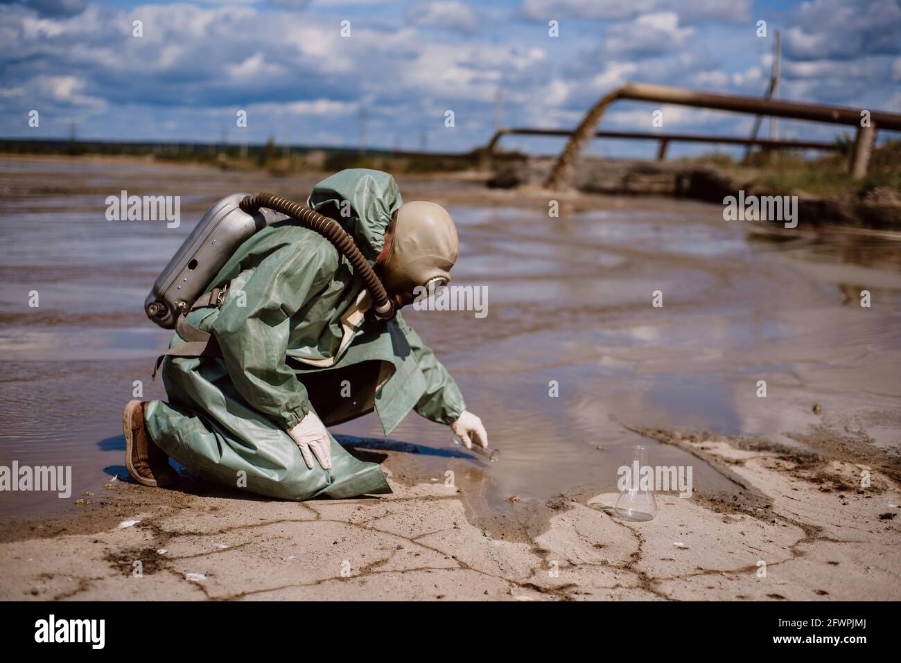 Un scientifique prélève un échantillon d'eau après le rejet de déchets chimiques. Un homme dans un respirateur et une combinaison de protection verte contre les radiations. Eau Banque D'Images